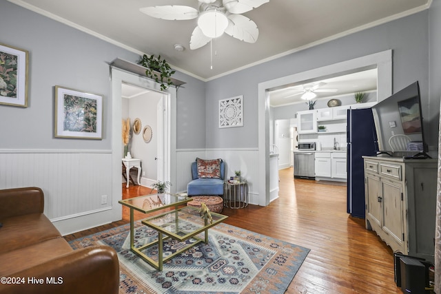 living room with ceiling fan, sink, ornamental molding, and light wood-type flooring