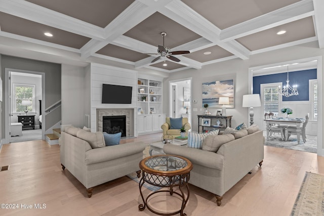 living room with beam ceiling, coffered ceiling, crown molding, ceiling fan with notable chandelier, and light wood-type flooring