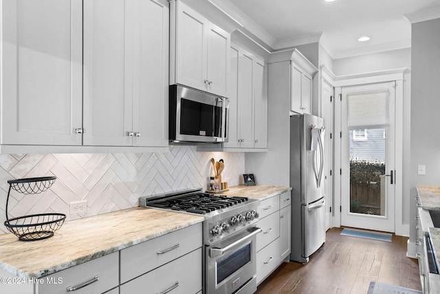 kitchen featuring white cabinets, dark hardwood / wood-style floors, light stone countertops, ornamental molding, and appliances with stainless steel finishes