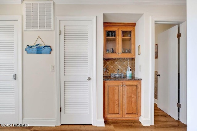 bar featuring ornamental molding, light wood-type flooring, dark stone countertops, and backsplash