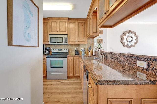 kitchen featuring appliances with stainless steel finishes, light wood-type flooring, backsplash, sink, and dark stone countertops