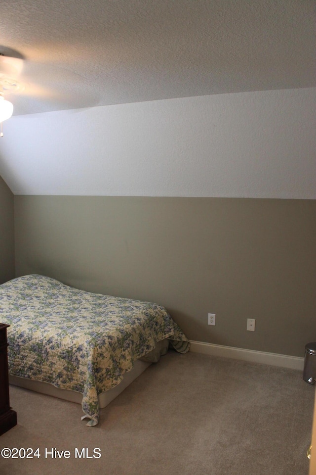 carpeted bedroom featuring a textured ceiling and vaulted ceiling