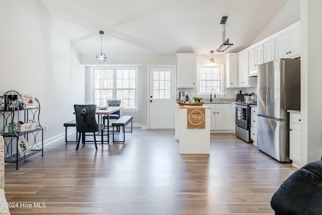 kitchen with white cabinets, appliances with stainless steel finishes, decorative light fixtures, and lofted ceiling