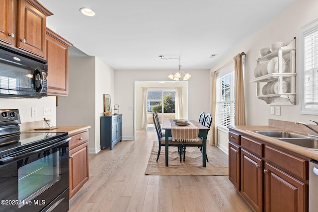 kitchen featuring sink, decorative light fixtures, a chandelier, light hardwood / wood-style floors, and black appliances