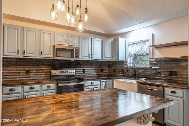 kitchen featuring butcher block counters, tasteful backsplash, a textured ceiling, lofted ceiling, and appliances with stainless steel finishes