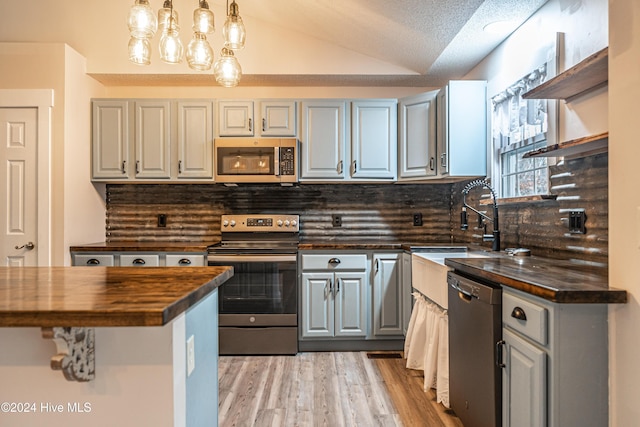 kitchen featuring gray cabinetry, tasteful backsplash, butcher block countertops, vaulted ceiling, and appliances with stainless steel finishes