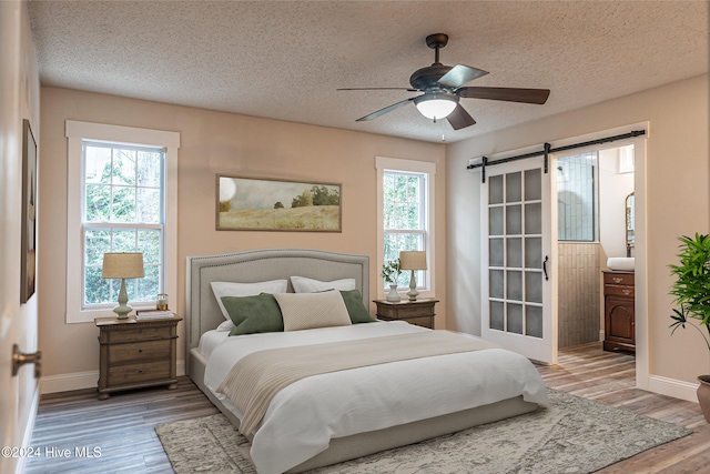 bedroom with wood-type flooring, a barn door, a textured ceiling, and ceiling fan