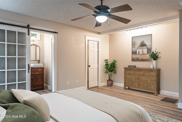 bedroom with ceiling fan, a barn door, wood-type flooring, and a textured ceiling