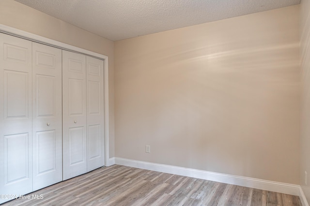 unfurnished bedroom featuring light wood-type flooring, a textured ceiling, and a closet