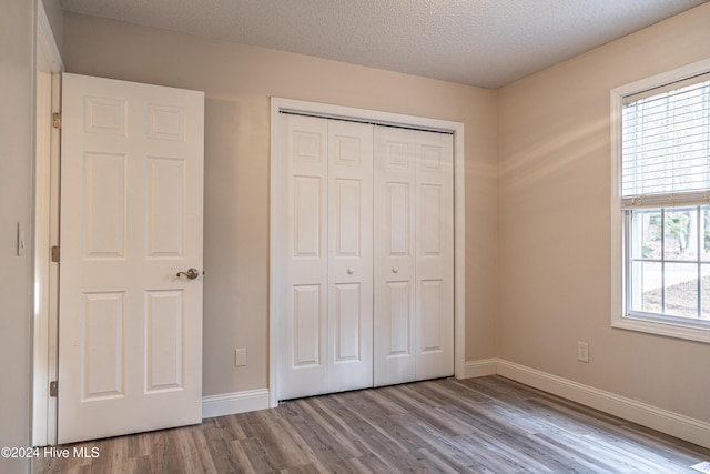 unfurnished bedroom with a textured ceiling, light hardwood / wood-style floors, multiple windows, and a closet