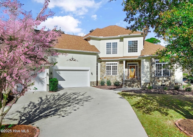 traditional home with stone siding, concrete driveway, an attached garage, a shingled roof, and a front yard