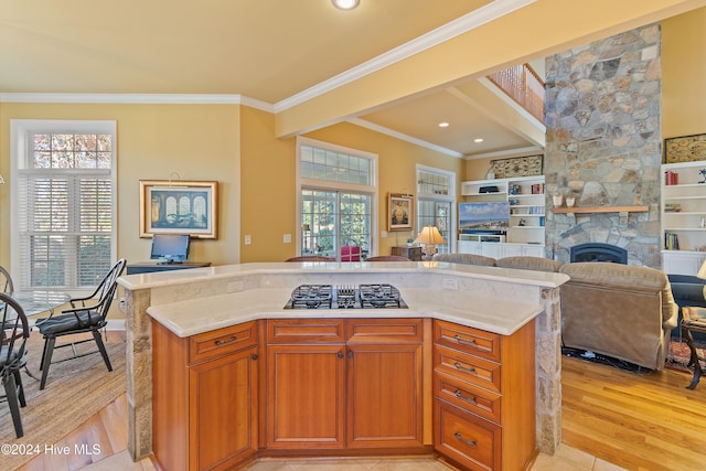 kitchen featuring crown molding, light wood-style flooring, open floor plan, a kitchen island, and a stone fireplace