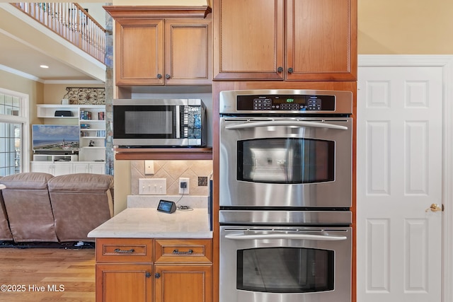 kitchen featuring light wood finished floors, stainless steel appliances, backsplash, ornamental molding, and open floor plan