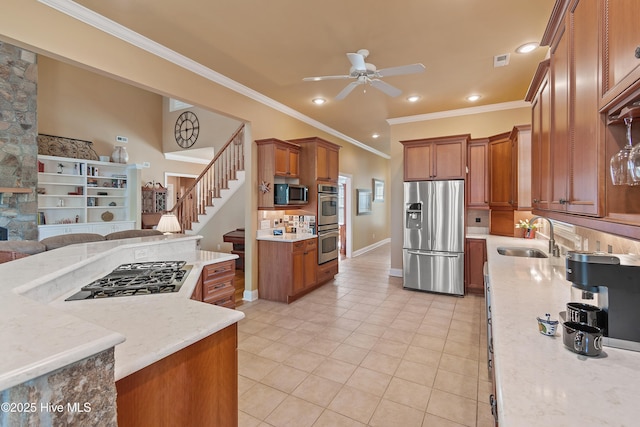 kitchen with stainless steel appliances, a sink, open floor plan, ceiling fan, and brown cabinetry