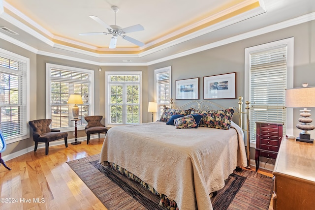 bedroom with wood finished floors, a tray ceiling, baseboards, ornamental molding, and visible vents