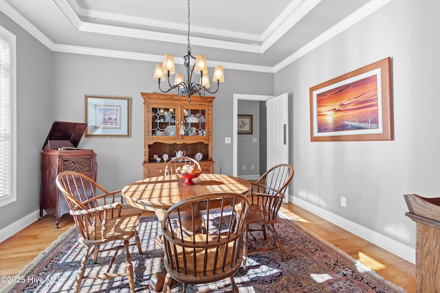 dining room featuring light wood finished floors, a tray ceiling, and ornamental molding