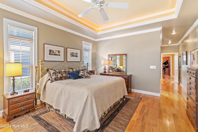 bedroom with a tray ceiling, light wood-style flooring, and multiple windows