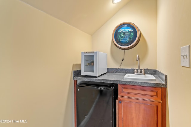 kitchen featuring lofted ceiling, a sink, brown cabinets, dishwasher, and dark countertops