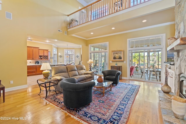 living room featuring crown molding, a towering ceiling, a stone fireplace, and light wood-type flooring