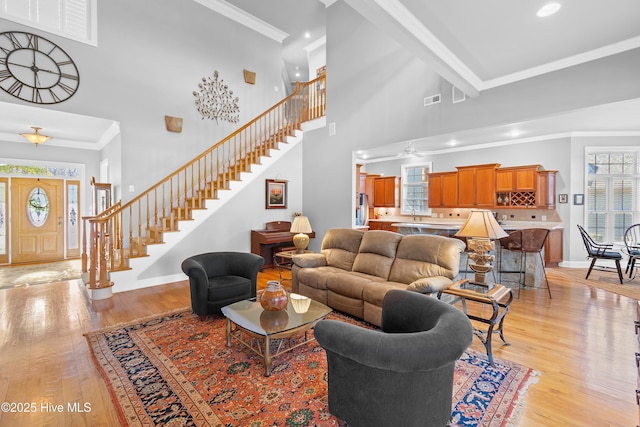 living area with stairs, ornamental molding, baseboards, and light wood-style floors