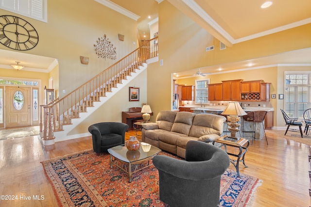 living room featuring crown molding, light hardwood / wood-style flooring, ceiling fan, and a high ceiling