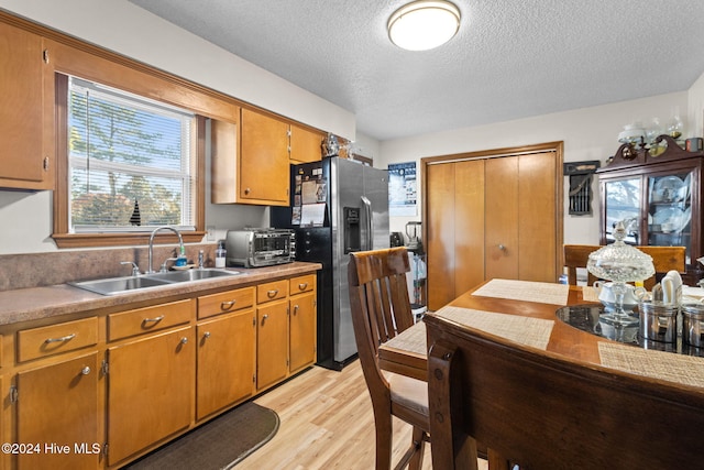 kitchen featuring stainless steel fridge, a textured ceiling, light hardwood / wood-style flooring, and sink