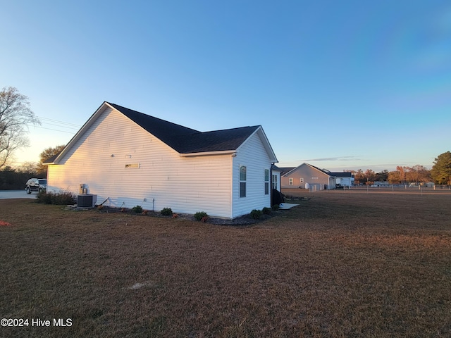 property exterior at dusk featuring a lawn and central AC unit