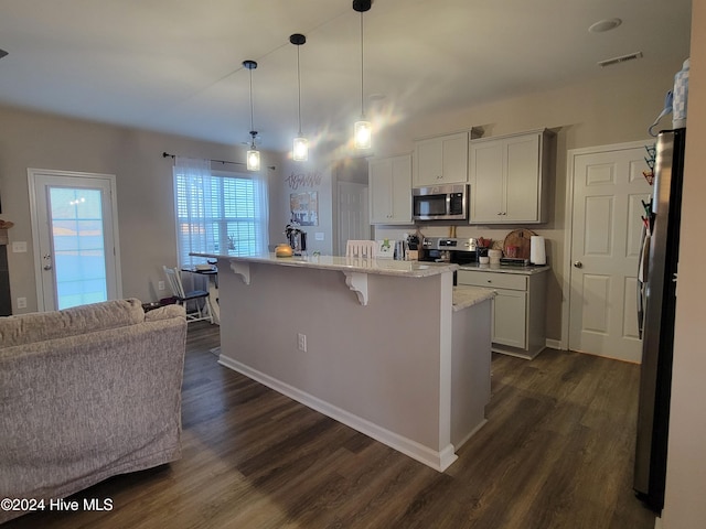 kitchen featuring a center island with sink, hanging light fixtures, dark hardwood / wood-style floors, appliances with stainless steel finishes, and a breakfast bar area