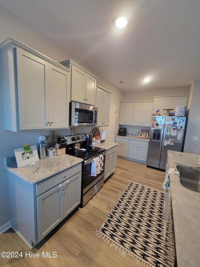 kitchen featuring light stone counters, sink, stainless steel appliances, and light hardwood / wood-style flooring