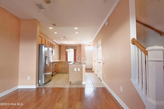 kitchen featuring appliances with stainless steel finishes, ornamental molding, decorative light fixtures, a center island with sink, and light hardwood / wood-style floors