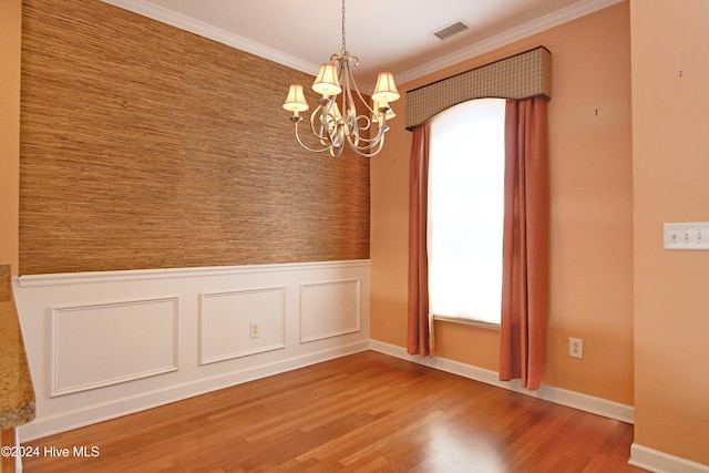 empty room with hardwood / wood-style floors, crown molding, and an inviting chandelier