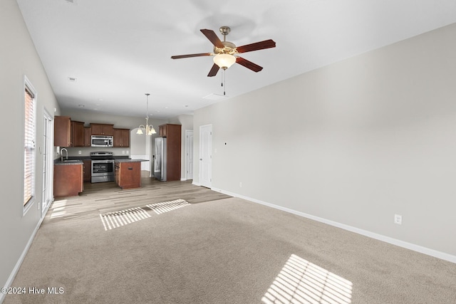 unfurnished living room with sink, light colored carpet, and ceiling fan with notable chandelier