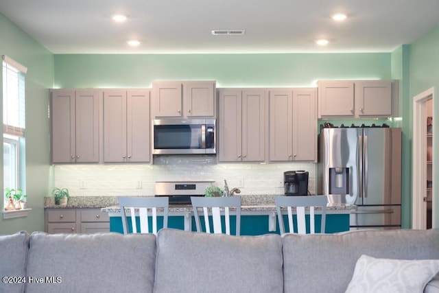 kitchen with tasteful backsplash, appliances with stainless steel finishes, and light stone countertops