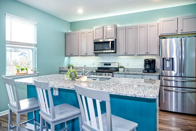 kitchen with gray cabinets, light stone countertops, appliances with stainless steel finishes, and a center island with sink