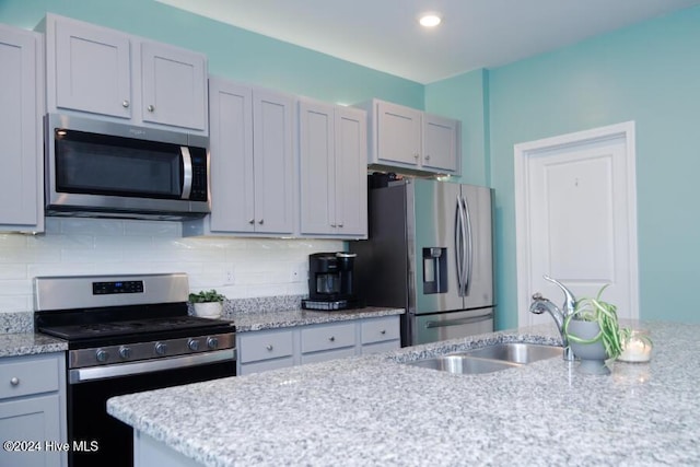 kitchen with appliances with stainless steel finishes, gray cabinets, sink, and backsplash