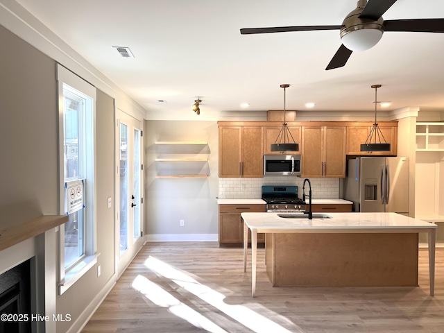 kitchen featuring tasteful backsplash, light hardwood / wood-style floors, pendant lighting, a kitchen island with sink, and appliances with stainless steel finishes