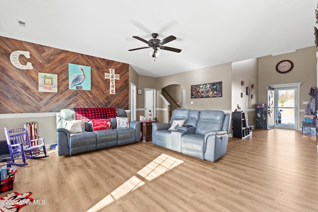 living room with wood walls, light hardwood / wood-style flooring, ceiling fan, and a high ceiling