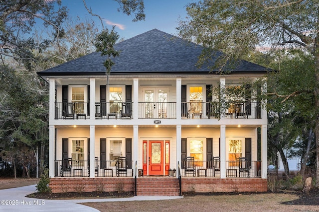 back house at dusk with a balcony and a porch