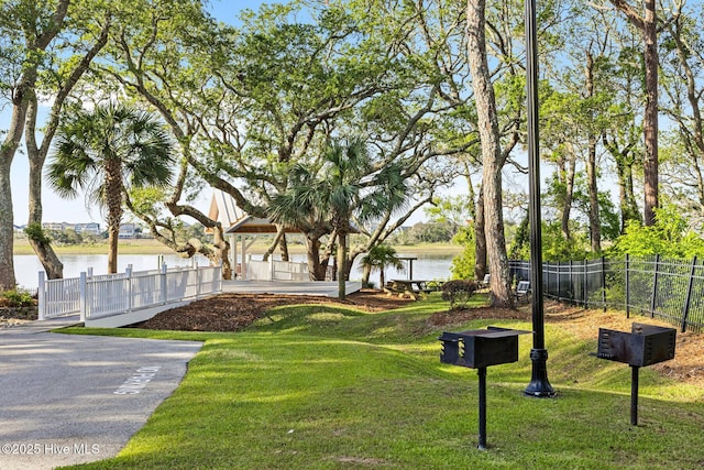 view of property's community with a lawn, a water view, fence, and a gazebo