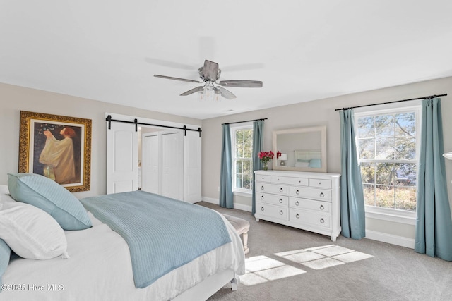 bedroom with ceiling fan, light carpet, and a barn door