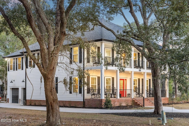 view of property exterior with a porch, driveway, roof with shingles, a balcony, and an attached garage