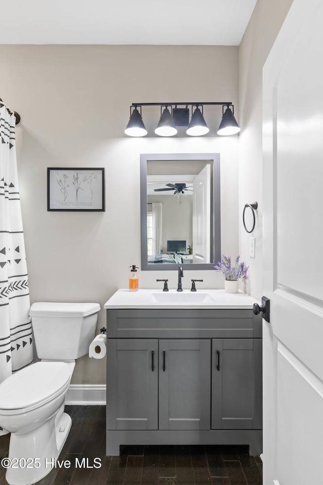 full bath with wood finish floors, vanity, toilet, a ceiling fan, and baseboards