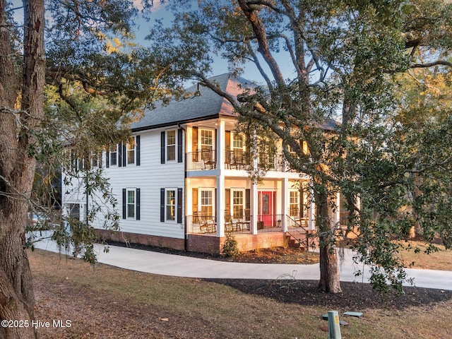 exterior space with roof with shingles, covered porch, driveway, and a balcony