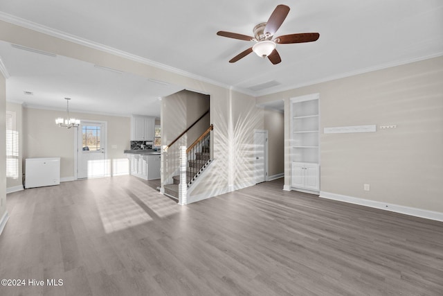 unfurnished living room with built in shelves, ceiling fan with notable chandelier, hardwood / wood-style flooring, and crown molding