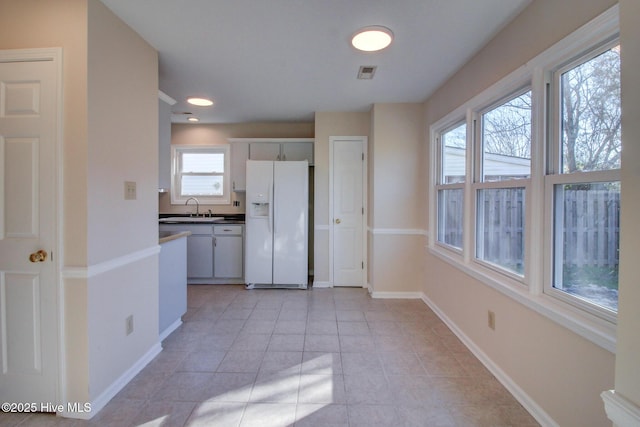 kitchen featuring white cabinetry, sink, white fridge with ice dispenser, and light tile patterned floors