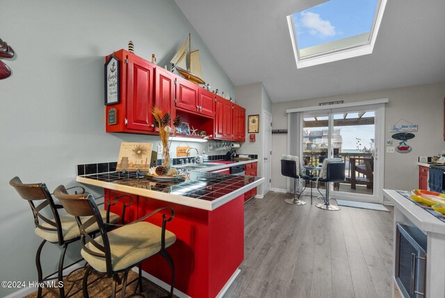 kitchen featuring tile countertops, lofted ceiling with skylight, sink, light wood-type flooring, and appliances with stainless steel finishes