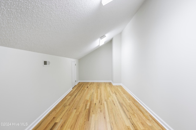 additional living space with hardwood / wood-style floors, a textured ceiling, and vaulted ceiling