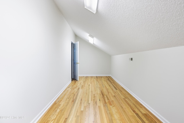 bonus room with a textured ceiling, light hardwood / wood-style flooring, and vaulted ceiling