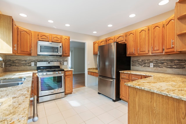 kitchen featuring light stone countertops, appliances with stainless steel finishes, backsplash, and sink