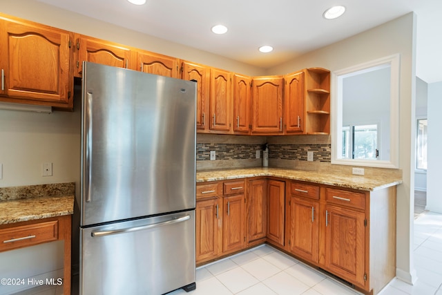 kitchen featuring light stone countertops, decorative backsplash, and stainless steel refrigerator